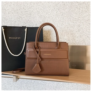Detail of brown crocodile pattern handbag with gold fashion lettering on a wooden shelf
