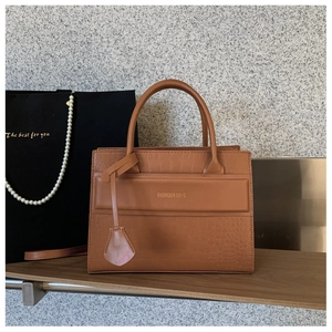 Detail of caramel tote bag with crocodile texture and fashion logo on wooden shelf