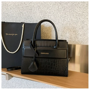 Detail of black crocodile embossed handbag with gold logo lettering on wood shelf