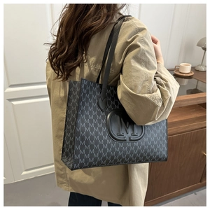 Detail view of large grey monogram tote bag with embossed M logo on khaki trench coat
