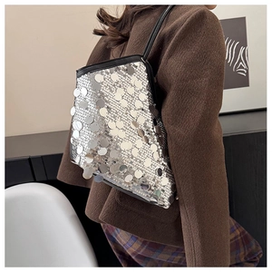 Detail of silver sequin shoulder bag with black strap worn by a model in a stylish interior