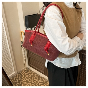 Detail of burgundy leopard embossed handbag with knot decor and smooth red handle strap