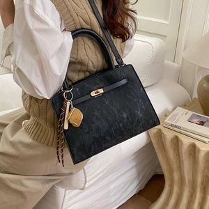 Classic black textured PU leather tote bag with gold buckle and creative charms on a sofa