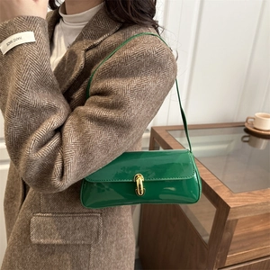 Sac baguette chic en cuir verni vert avec fermoir doré porté par un mannequin