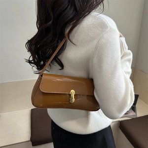 Sac bandoulière en cuir verni caramel avec boucle dorée porté par un mannequin