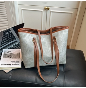 Detail of grey-green tote bag with brown leather handles placed on a black leather bench