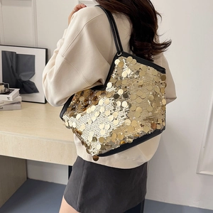 Large gold sequin tote bag with black leather straps shown in a modern interior setting
