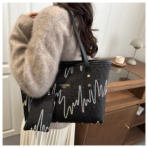 Close-up of black tote bag with colorful wave embroidery and brand metal logo