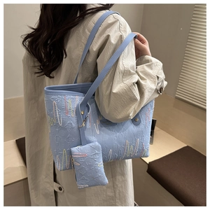 Detail view of light blue tote bag with letter embossing and wave embroidery worn by model
