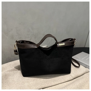 Detail of a black suede tote bag with brown leather handles and gold metal hardware