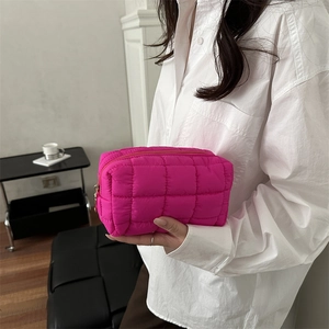 Bright pink quilted down cosmetic bag with zipper closure held by a model in casual style
