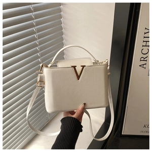Détail du sac blanc cassé à texture litchi et boucle métallique dorée en forme de V
