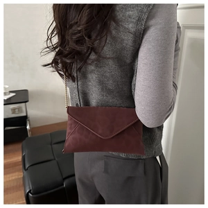 Detail of burgundy envelope chain bag worn over the shoulder showing premium suede texture