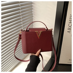 Détail du sac à main bordeaux avec garniture dorée en V et texture cuir grainé