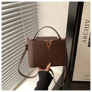 Détail du sac à main en cuir marron foncé avec accent métallique en V doré et texture grainée