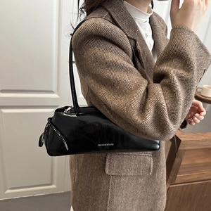 Borsa sottospalla nera lucida con scritta bianca indossata su un blazer a spina di pesce