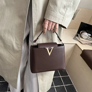 Chic sac à main marron foncé en cuir avec boucle V dorée et poignée porté par un modèle