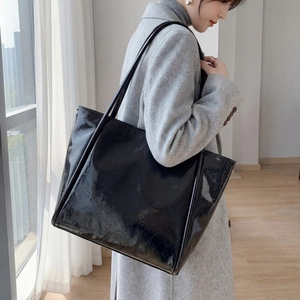 Large black glossy leather tote bag for women shown as a stylish shoulder bag on a model