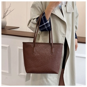 Detail of dark brown woven tote bag paired with a khaki trench coat for an autumn look