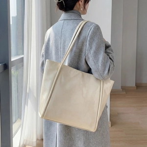 Detail view of large cream patent leather tote bag showing glossy texture and shoulder straps