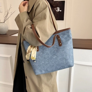 Blue denim tote bag with brown leather trim and silk scarf detail worn by a model