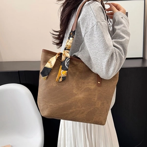 Brown leather tote bag with silk scarf accessory worn by a model in a modern home setting