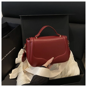 Close-up of a red saddle bag on white silk with a stylish wide fabric shoulder strap
