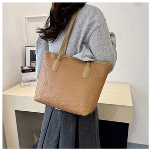 Caramel faux leather tote bag with woven texture worn by model in a minimalist setting