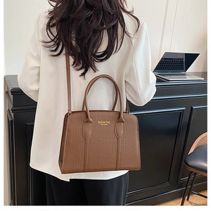 Rear view of brown croc-embossed tote bag worn by model in a modern office setting