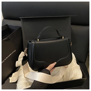 Detail of black saddle bag with wavy flap, gold hardware, and cream woven strap in gift box