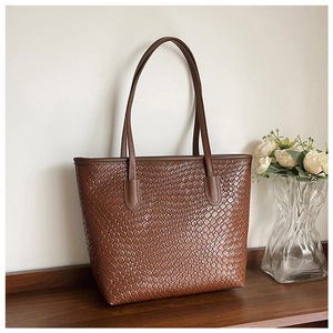 Close-up of a deep coffee tote bag with woven texture on a wooden desk with flowers