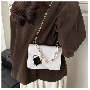 Detail of white faux leather small square bag with gold chain strap on model's shoulder