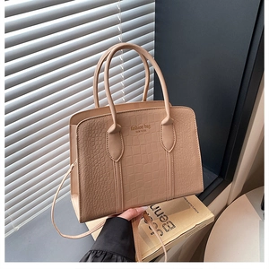 Detail of beige crocodile embossed texture and dual handles on a stylish Boston bag