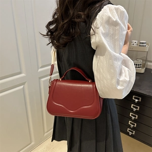 Red leather handbag for women featuring curved stitching and a wide fabric shoulder strap