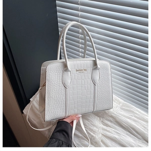 Detail view of white crocodile embossed leather bag with golden fashion text and top handle