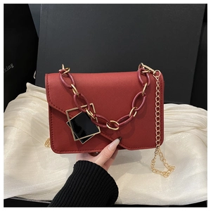 Close-up of deep red square handbag featuring acrylic chain and geometric pendant