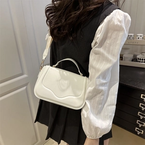 Chic white leather handbag with wave textured flap shown as a crossbody on a model