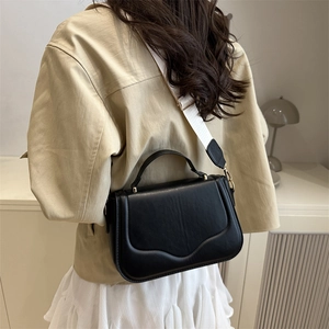 Women's black leather crossbody bag with cream wide strap shown on a female model