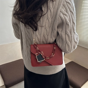 Chic red chain crossbody bag worn by model over a beige knit sweater in a stylish interior