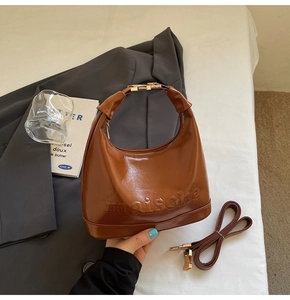 Close-up of brown crescent PU leather handbag featuring embossed lettering and gold hardware