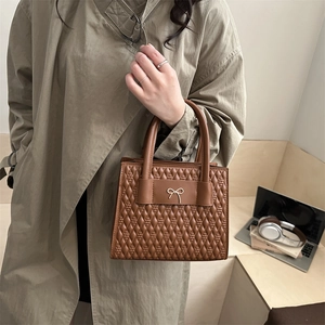 Sac fourre-tout matelassé marron caramel avec nœud doré dans un cadre professionnel