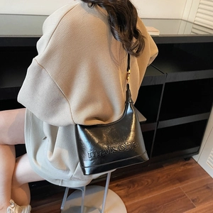 Elegant black glossy leather handbag with embossed lettering on a stylish model