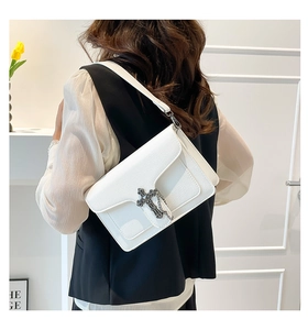 Macro detail of white pebble leather texture and silver cross emblem on a shoulder bag
