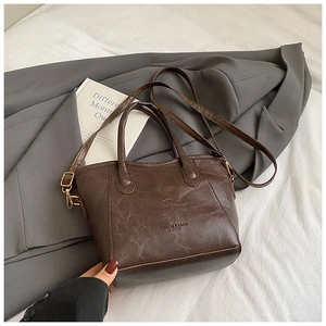 Detalle de bolso tipo cubo marrón oscuro con herrajes dorados y logotipo grabado