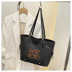 Detail of black tote bag featuring brown plush DMT AOTO letter patches and gold hardware
