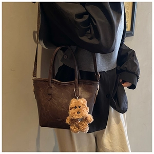 Detail of vintage brown leather bucket bag featuring a plush bear charm and long strap
