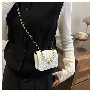 Mini white woven crossbody bag with pearl handle and gold chain strap in home setting