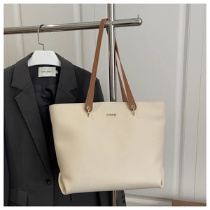 Detail of cream tote bag with brown straps and metallic logo on office blazer background