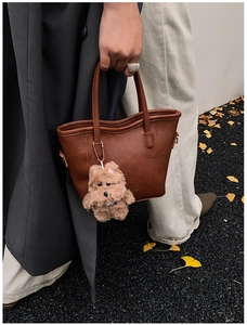 Bolso cubo de cuero sintético marrón con colgante de perro sobre hojas de ginkgo