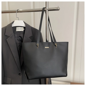 Detail of minimalist black leather tote bag with gold metal plaque and long straps